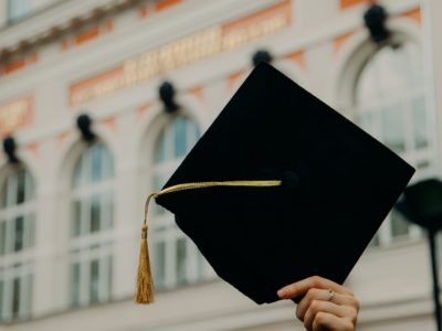 Graduation cap held in air in front of building