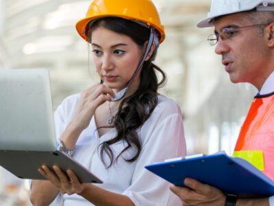 An engineering major in an orange hard hat looking at a laptop with her coworker.