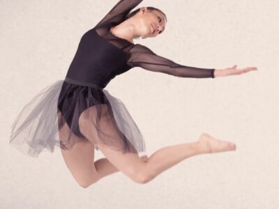 A girl in a black dance outfit jumping and posing in the air